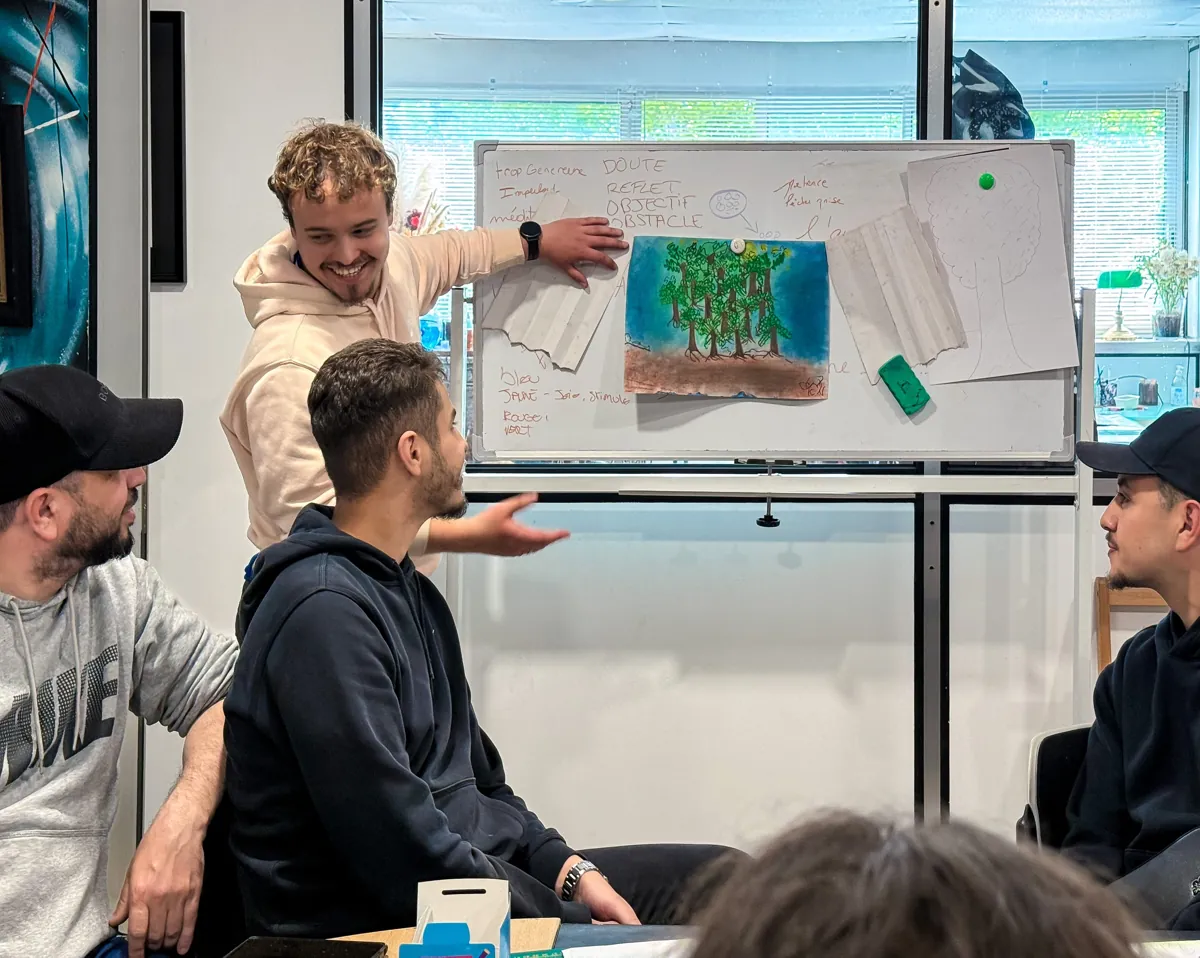 Un participant présente son croquis au tableau devant son équipe
